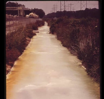 A contaminated sewage drainage ditch is seen behind Pittsburgh Glass Company in the early 1970s. | The U.S. National Archives