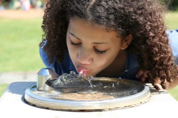 Little girl at a drinking fountain outside. | Photo: Amy Kober