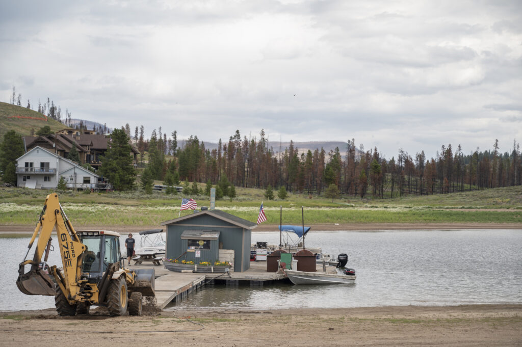 A backhoe pushes the dock store further out into what’s left of Lake Granby | Photo by Tim Romano
