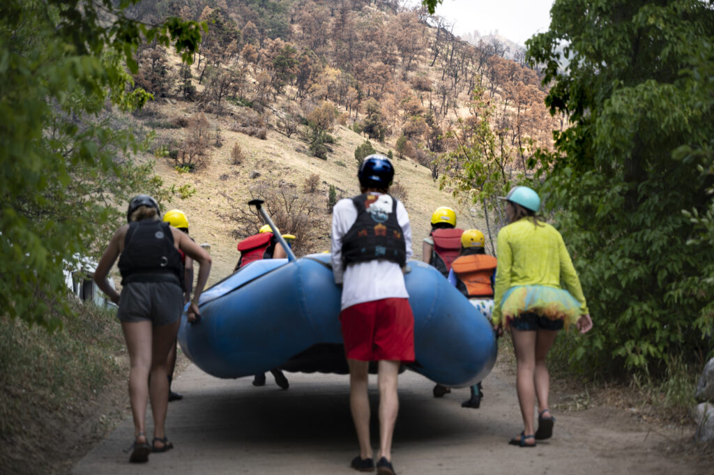 Raft guides and clients walk a boat out of the sediment laden waters of the Colorado at the Grizzly Creek Rest Area in Glenwood Canyon on the Colorado | Photo by Tim Romano
