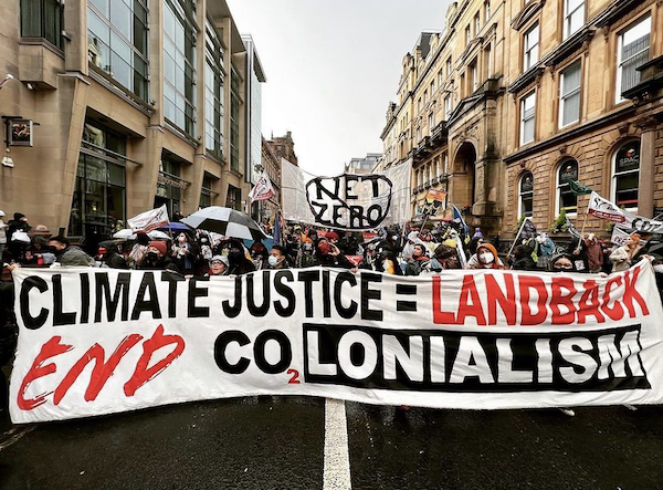 Protestors at COP26 holding a banner reading "Climate Justice = Land back"